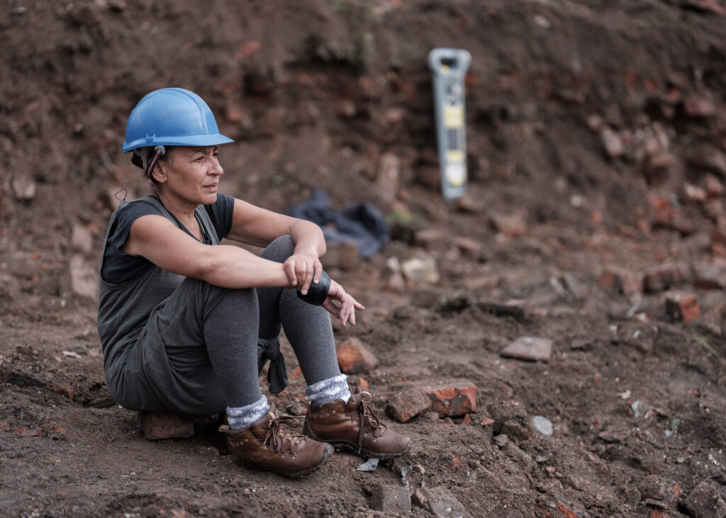 Image: Linda Brogan Linda Brogan in a builder's hat sat on a brick at excavation of the Reno surrounded by rubble