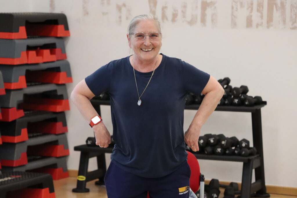 A woman smiling at the camera with hands on hips as she participates in fitness class. 