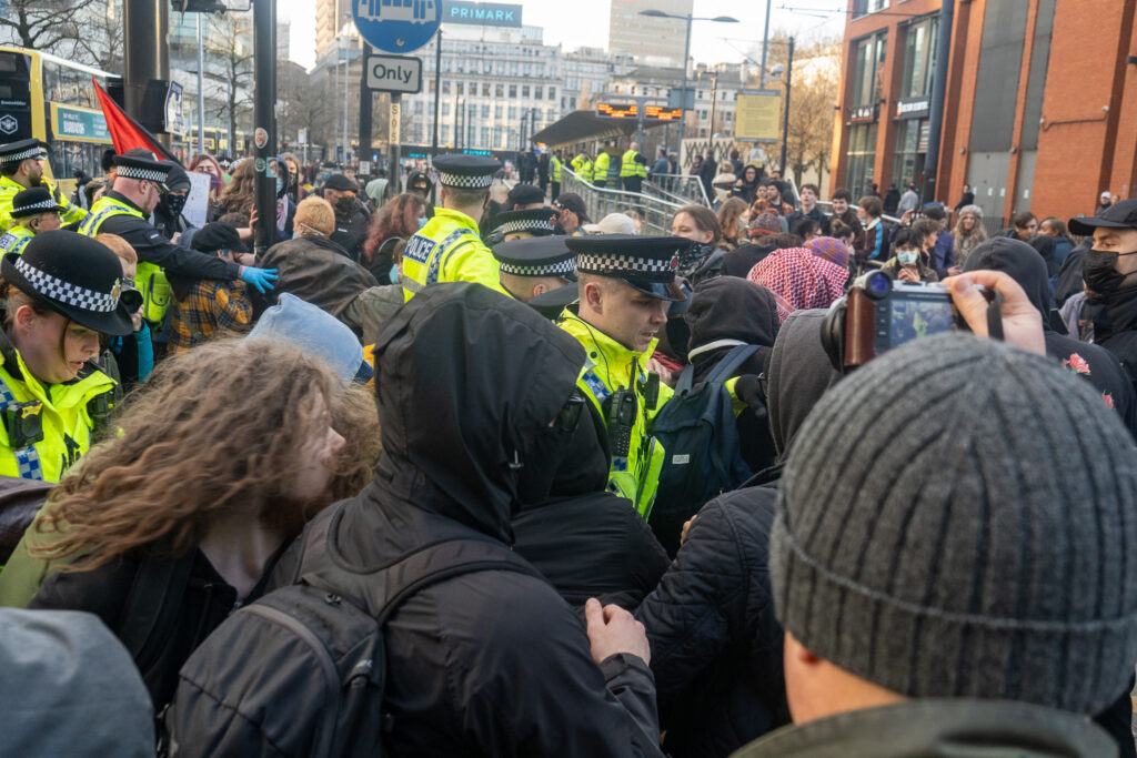 A crowd of people in Piccadilly Gardens, interspersed with police officers wearing high-vis jackets.