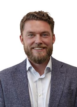 Phil Eckersley is a white man with wavy ginger hair and a beard. He is wearing a suit and no tie, and is smiling at the camera.